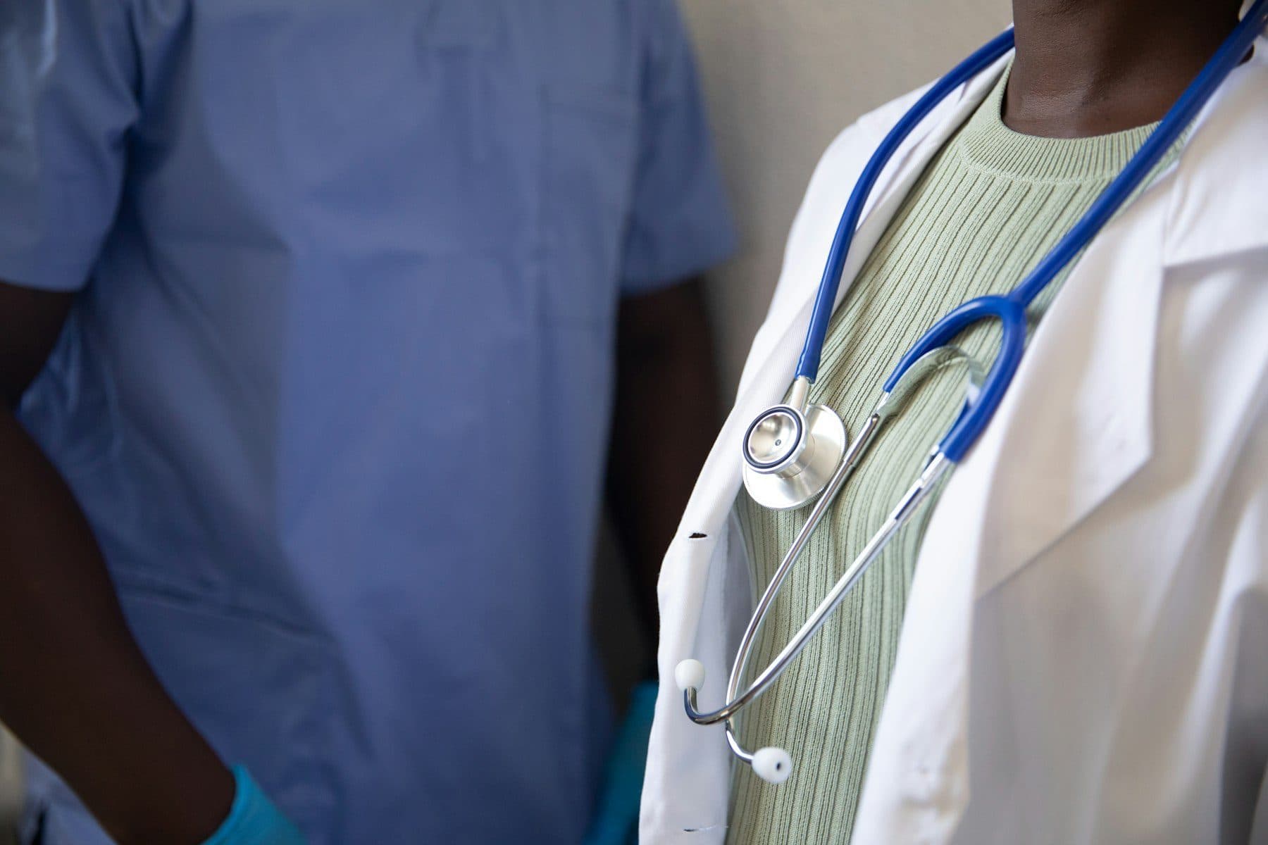 A clinician in a white coat with a stethoscope, beside a colleague in scrubs.