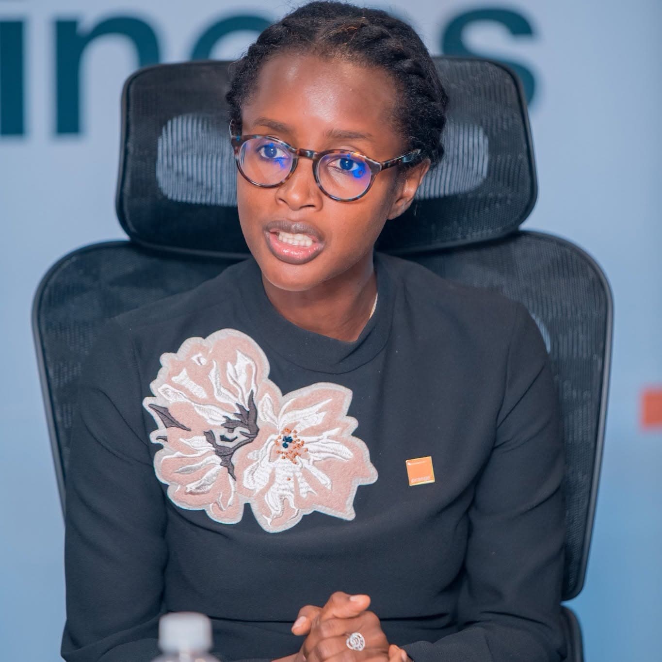 A woman seated at a boardroom table, speaking.