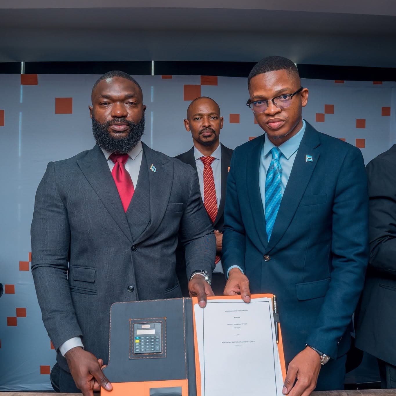 Two men holding open a folder containing the signed memorandum, facing the camera.