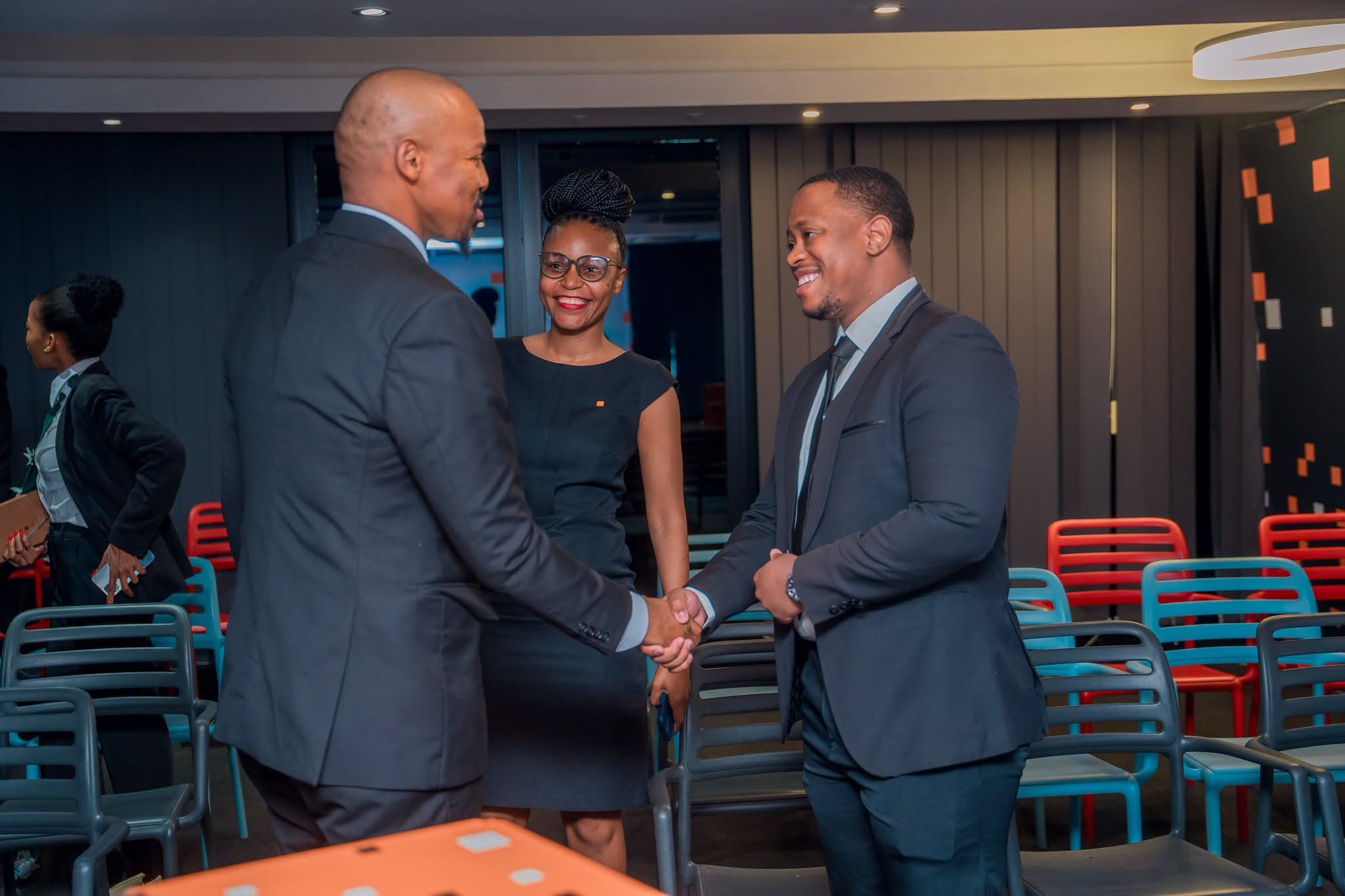 Two men shaking hands beside a colleague in a meeting room before the ceremony.