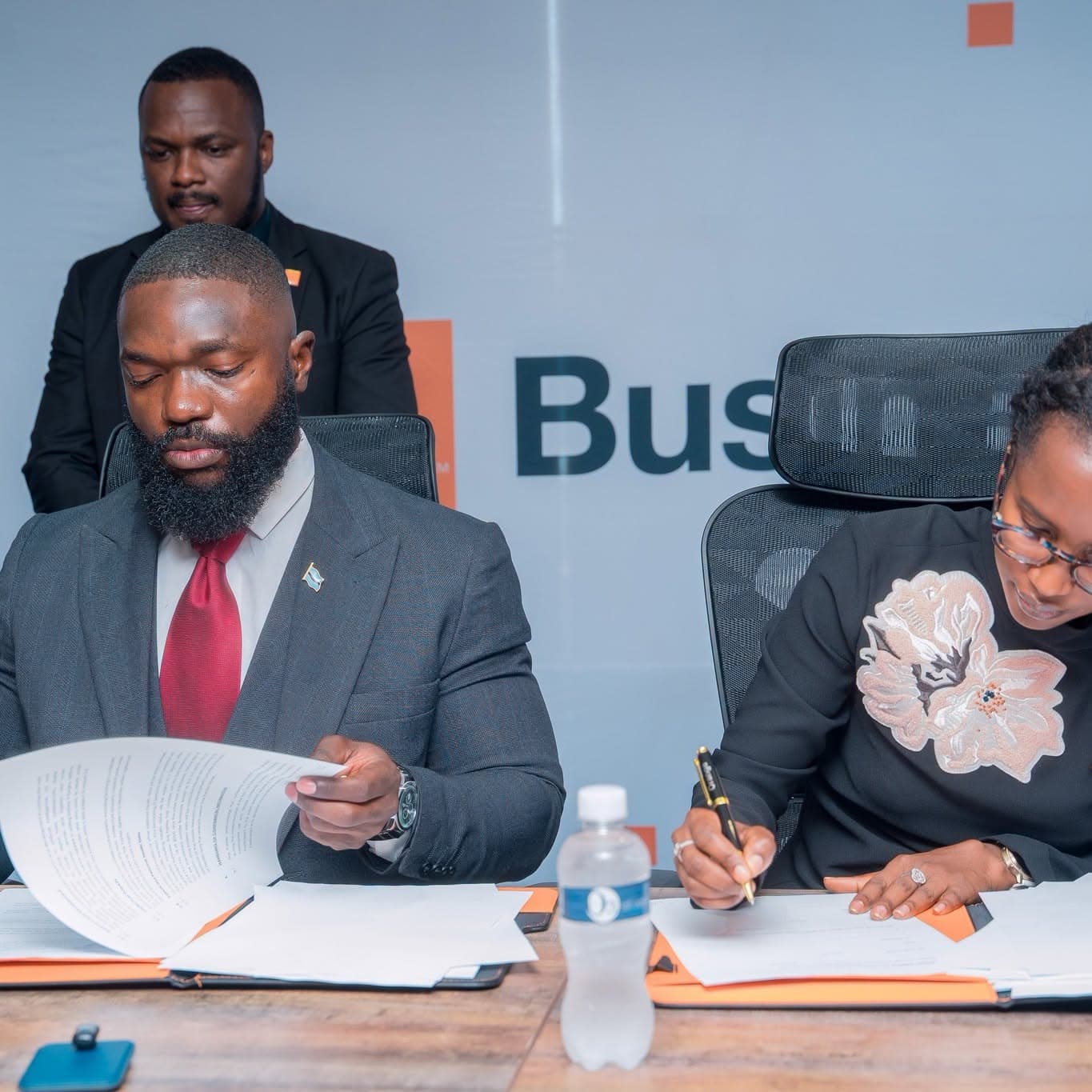 A man and a woman seated at a boardroom table, signing documents.