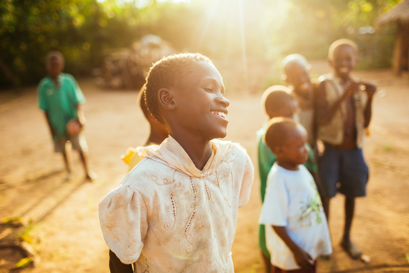 Children outdoors in late afternoon light, one of them laughing towards the camera. Paediatric and neonatal intensive care and children's surgery are planned services at TEMCO, opening 2029.